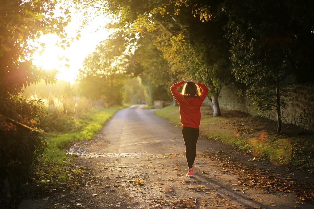 Frau mit roter Sportjacke, die einen Feldweg entlang geht. 