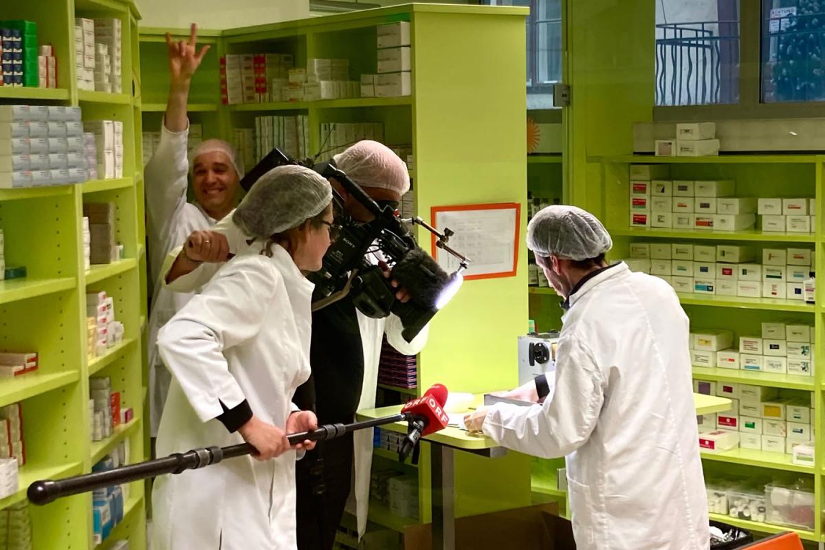 Ein ORF-Team filmt den gehörlosen PKA David Iberer in der Verblisterung der Marien Apotheke Wien. Im Hintergrund steht Mag. Sreco Dolanc und zeigt das I Love You Zeichen in Gebärdensprache - das internationale Solidaritätssymbol für Gehörlose.