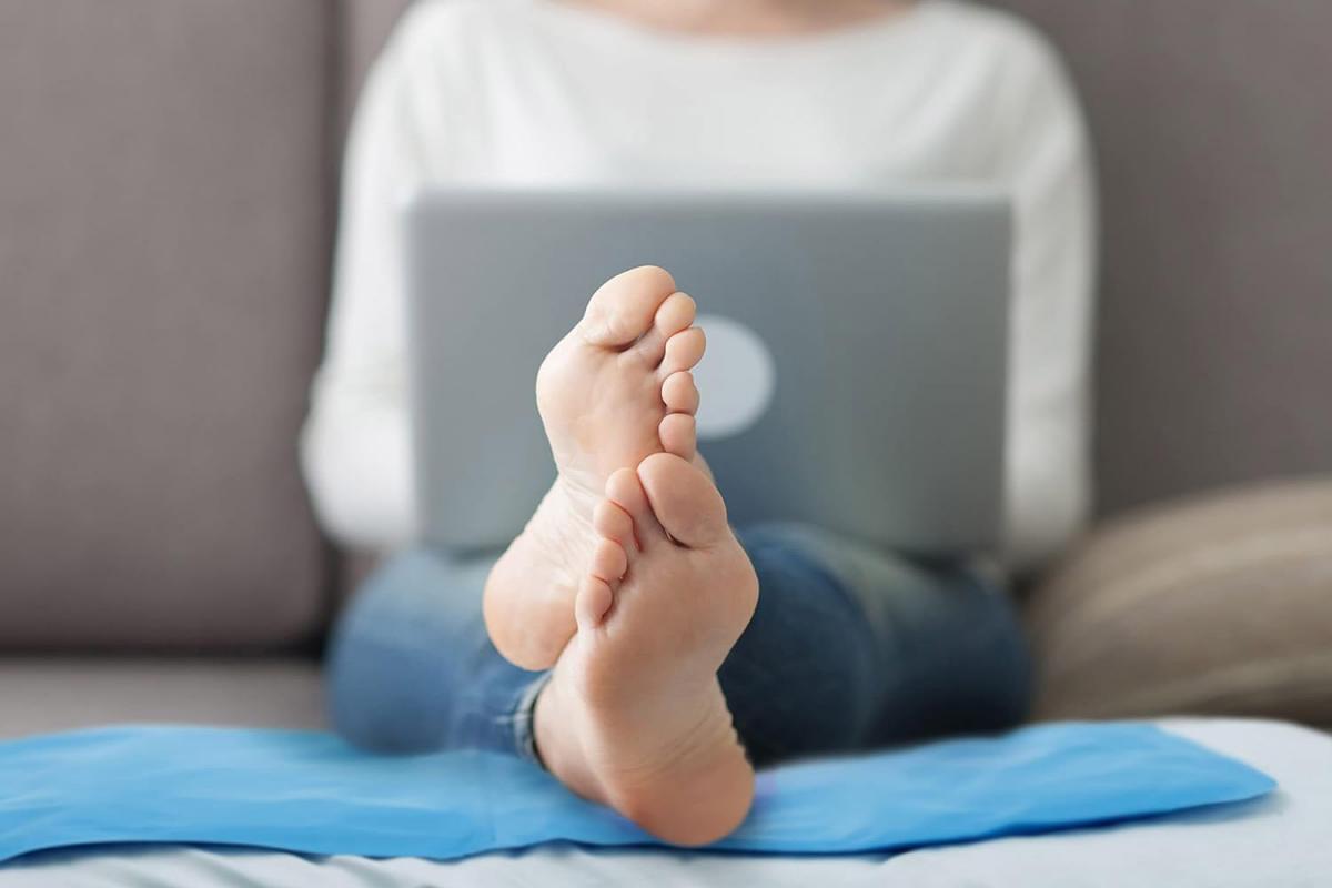 Bramble kühlendes Gelkissen als Fußunterlage für eine Frau, die auf der Couch sitzt und einen Laptop auf dem Schoß hat.